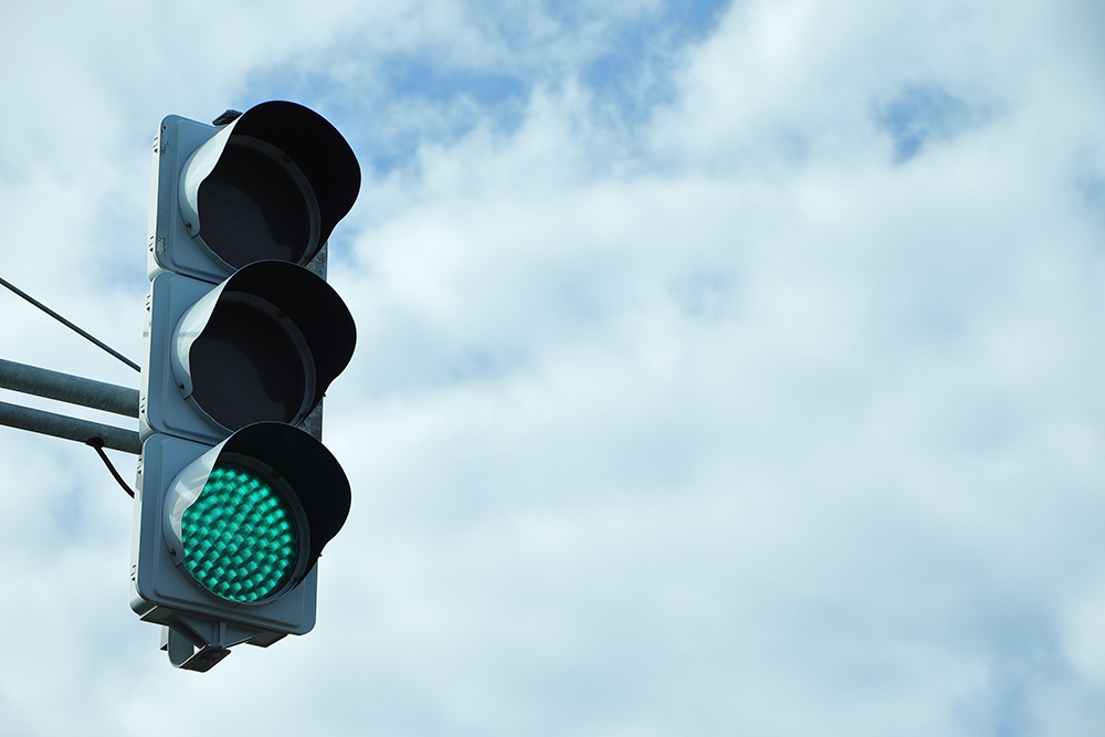 A traffic light with the green light illuminated against a cloudy sky background.