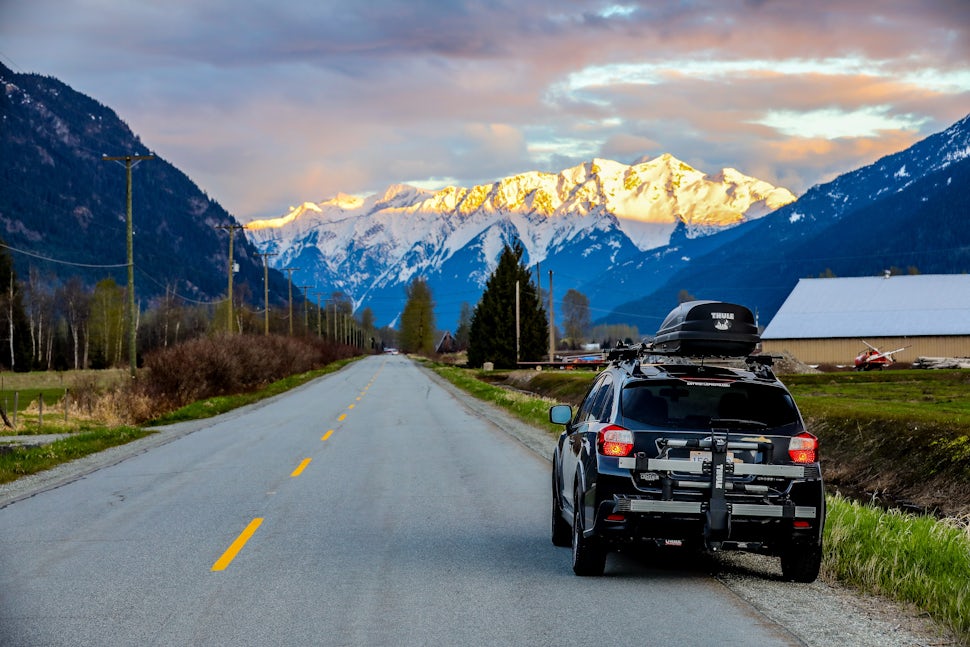 A road leading towards snow-capped mountains with a parked SUV on the roadside