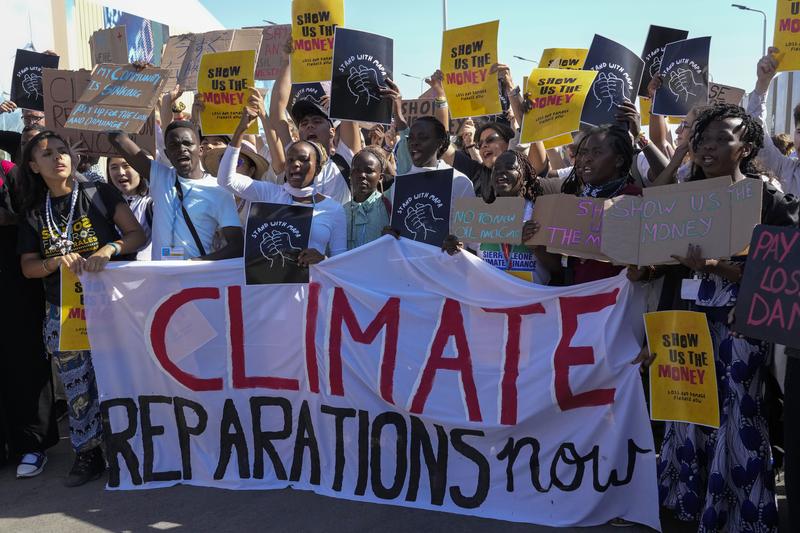 Protesters holding signs demanding climate reparations and action.